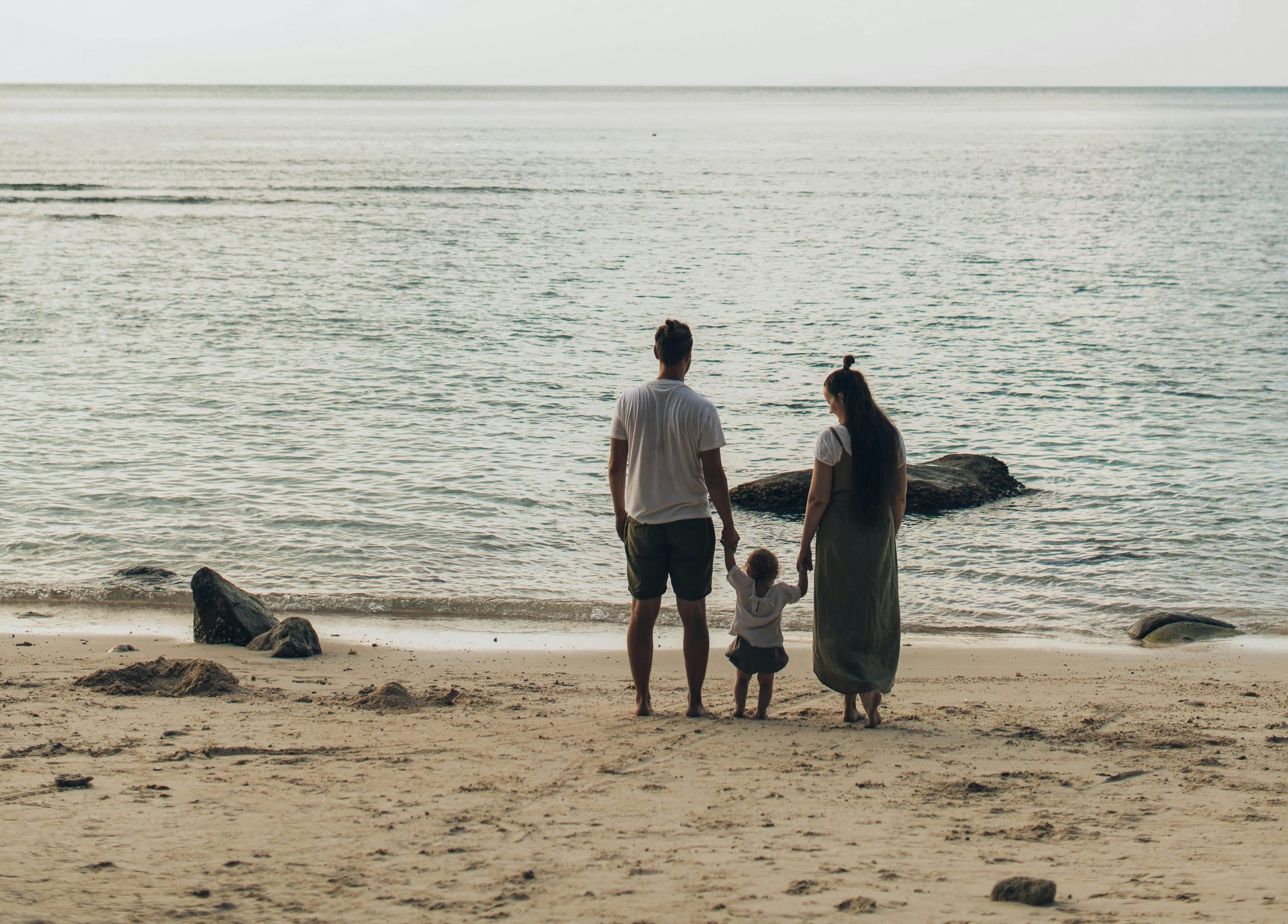 A family with a young child stands together on a quiet beach looking out at the ocean, symbolising the personal impact and decisions involved in avoiding common mistakes when cancelling a dependent visa.